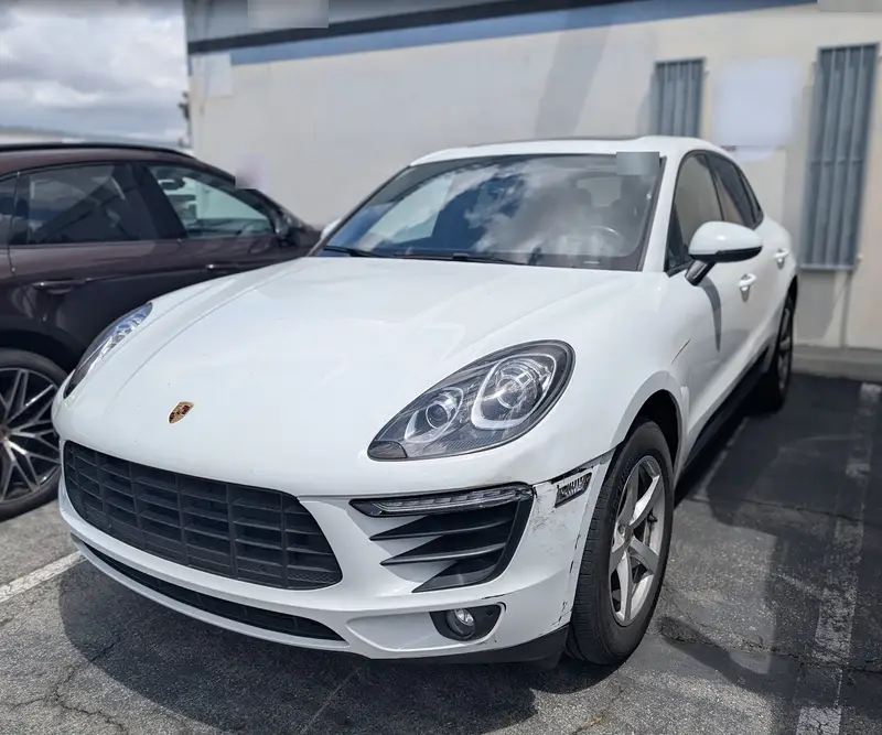 White 2018 Porsche Macan with a cracked and scraped front bumper corner by the left front wheel, before repair