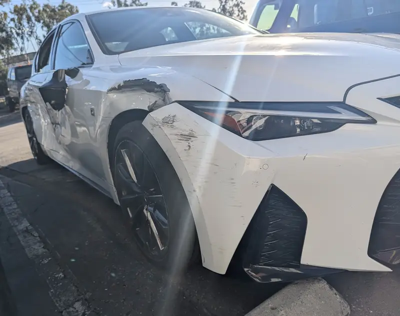 White 2024 Lexus IS 350 F SPORT with scrapes on the right front bumper and fender and dents along the right doors, before repair