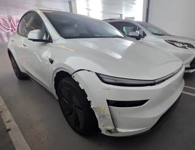 White 2026 Tesla Model Y with a torn right front fender and a scraped front bumper corner, before repair